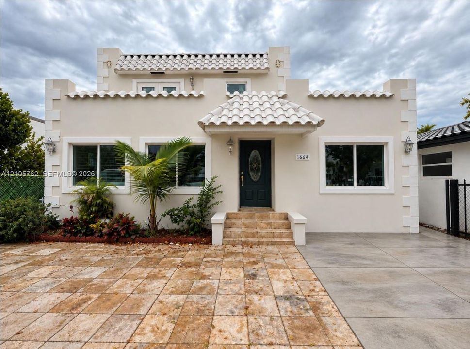 Stucco exterior featuring mission-style roof tiles, decorative corner quoins, stone-finish entryway steps, and a paved stone driveway
