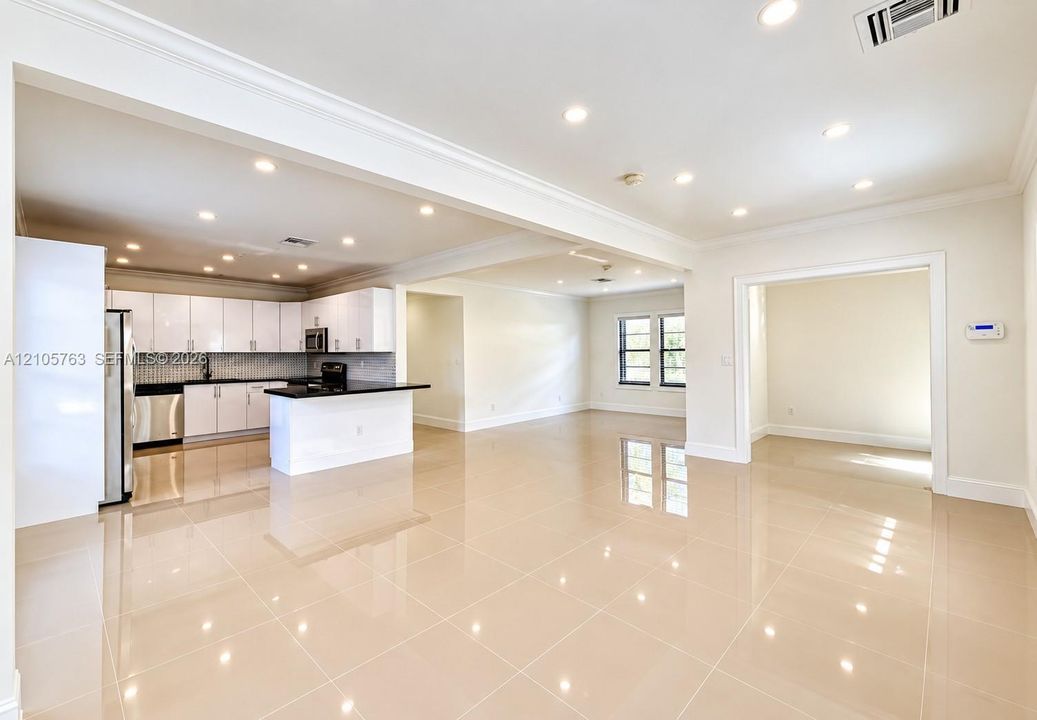 Open-concept interior featuring large-format tile flooring, recessed ceiling lighting, crown molding, a kitchen island with stone countertops, and crisp white cabinetry