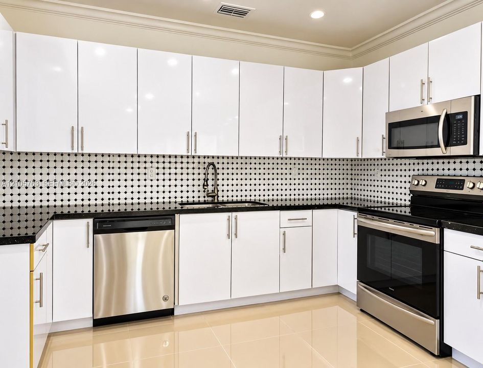 Kitchen featuring high-gloss white cabinetry, dark stone countertops, stainless steel appliances, a geometric tile backsplash, and polished tile flooring