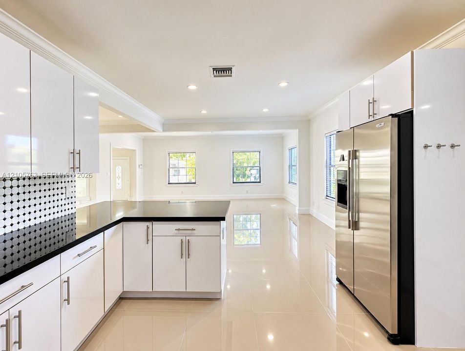 Kitchen featuring white gloss cabinetry, dark stone countertops, stainless steel refrigerator, patterned tile backsplash, and polished tile flooring
