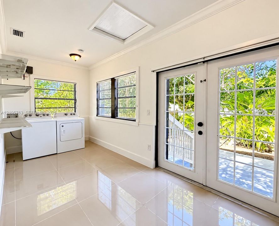 Utility room featuring large-format tile flooring, dual-pane windows, crown molding, and glass-paneled double doors providing exterior access