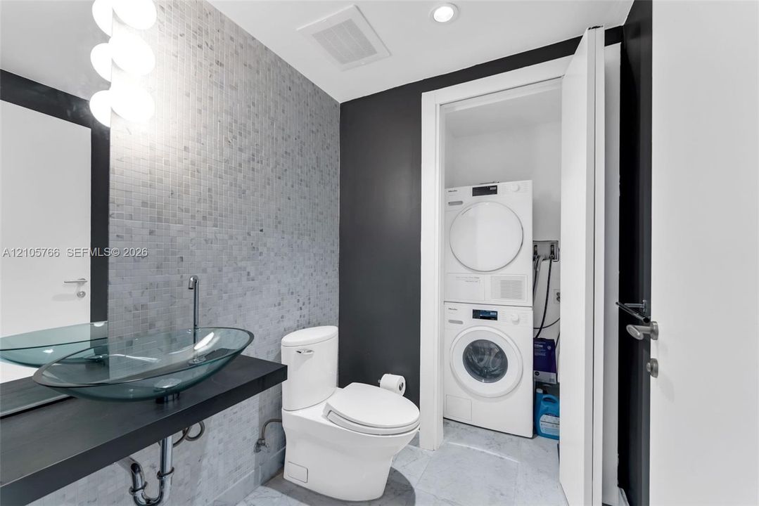 Half bath with glass vessel sink, mosaic tile and the stacked Miele washer and dryer.