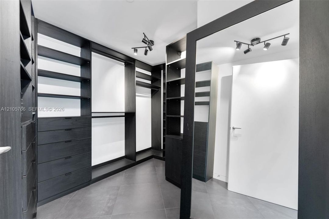 Primary walk-in closet with built-in drawers, shelving, hanging space and a floor mirror.