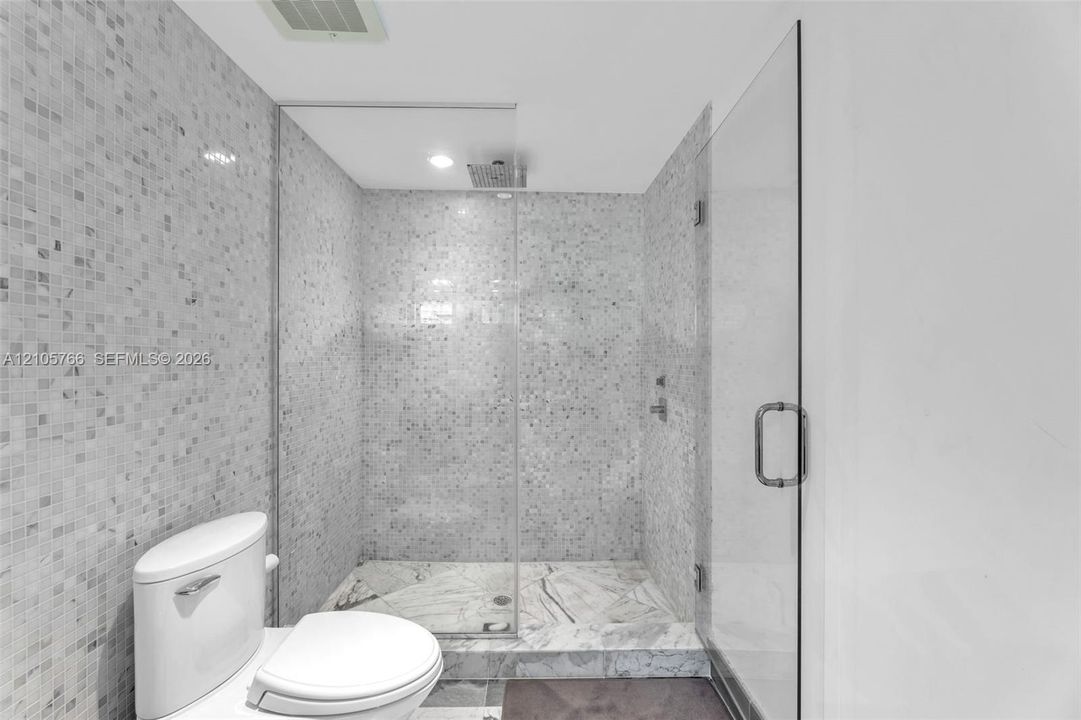 Primary bath with a glass-enclosed walk-in shower, rain shower head and mosaic tile walls.