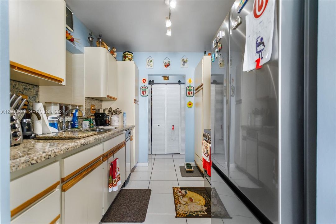 Kitchen featuring light-toned cabinetry, stone-patterned countertops, stainless steel refrigerator, white ceramic floor tile, and a sliding barn-style door