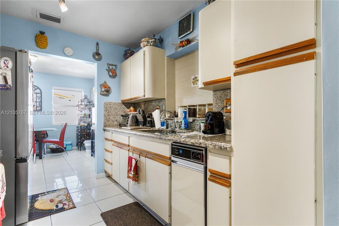 Kitchen featuring stone-finish countertops, tile flooring, cabinetry with wood trim, and stainless steel dishwasher