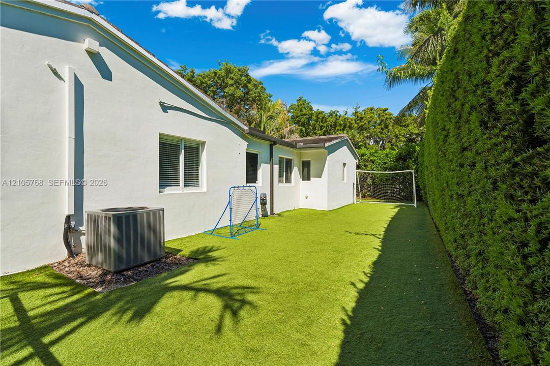 Side yard featuring synthetic turf, tall privacy hedges, and white stucco exterior walls