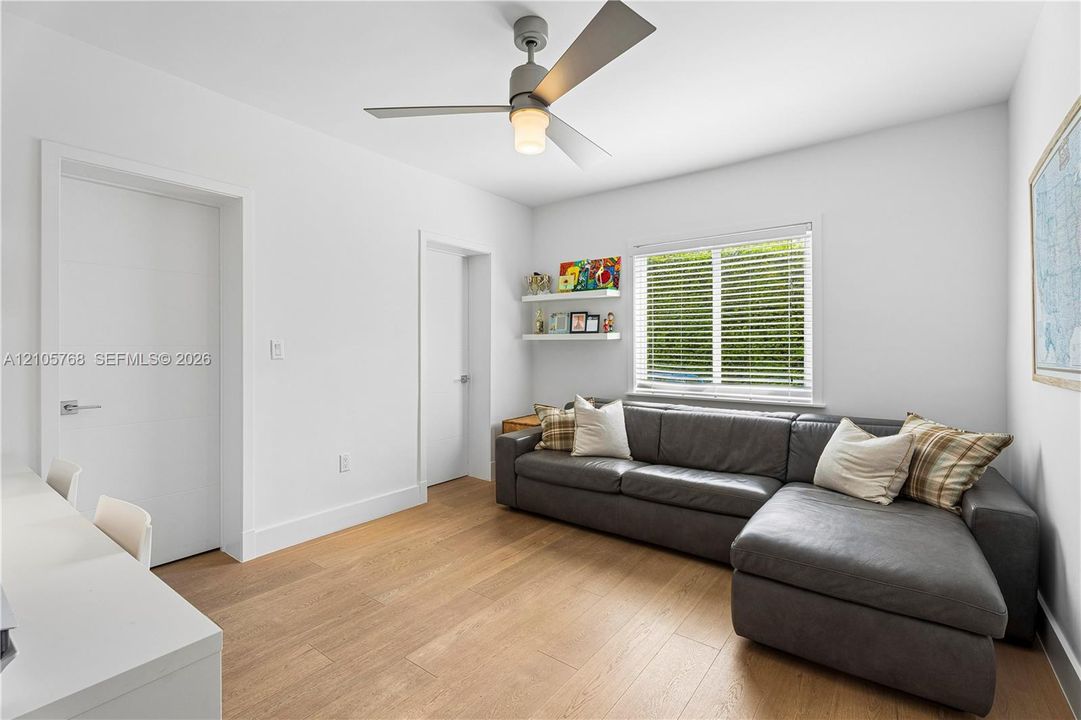 Wood-finish flooring, ceiling fan with integrated light fixture, two built-in wall shelves, and horizontal window blinds