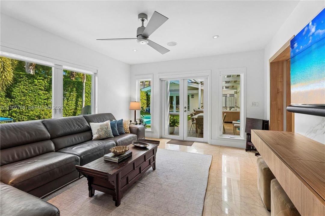 Bright living space featuring stone flooring, a ceiling fan, custom wood-finish built-in cabinetry, and multi-panel glass doors