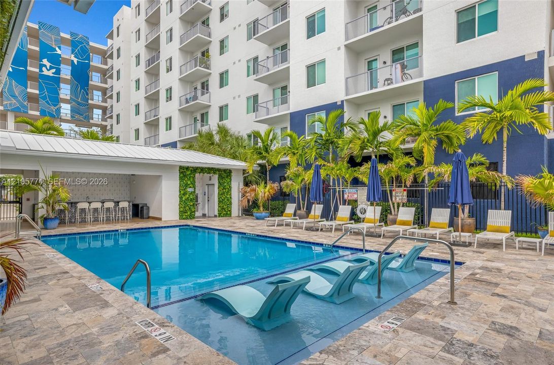 Swimming pool with tanning ledge, built-in poolside cabana with bar seating, and stone-paver decking