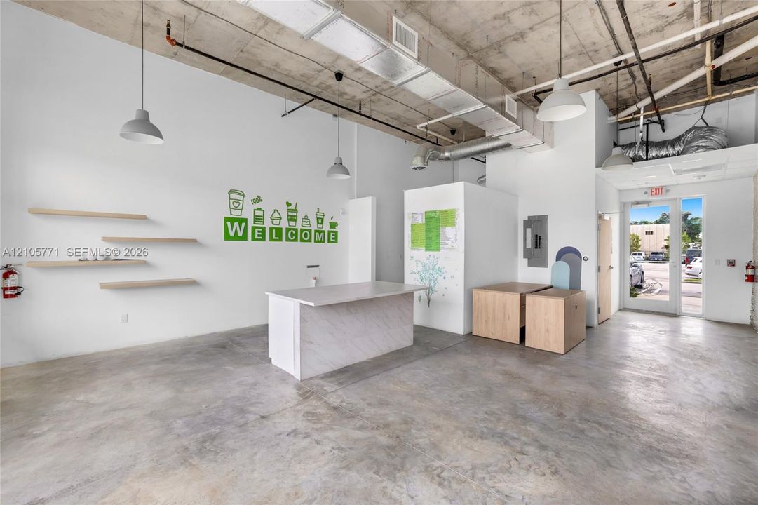 Industrial-style interior featuring exposed concrete ceilings with structural ductwork, polished concrete flooring, built-in reception counter with stone-finish surfacing, and wall-mounted wooden display shelving