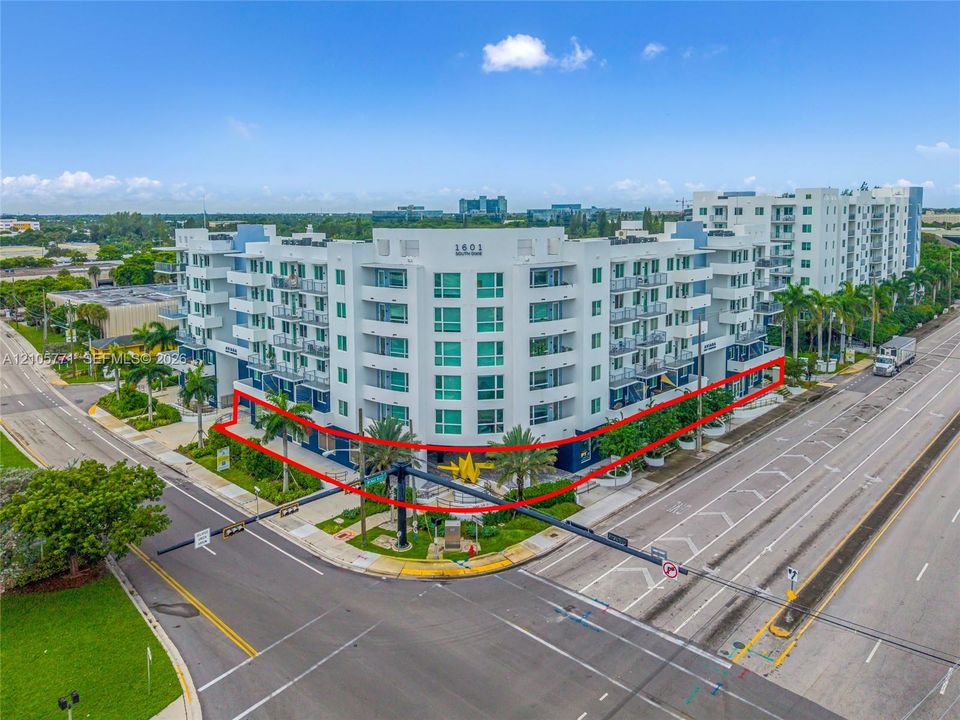 Multi-story commercial building featuring a white facade, glass-paneled balconies, corner orientation, and ground-level retail storefronts