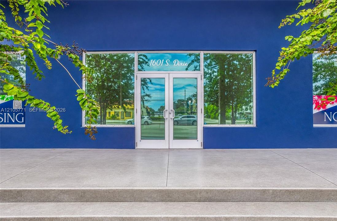 Exterior facade featuring a smooth blue finish, expansive glass storefront windows, double-entry glass doors with brushed metal hardware, and a poured concrete entrance platform