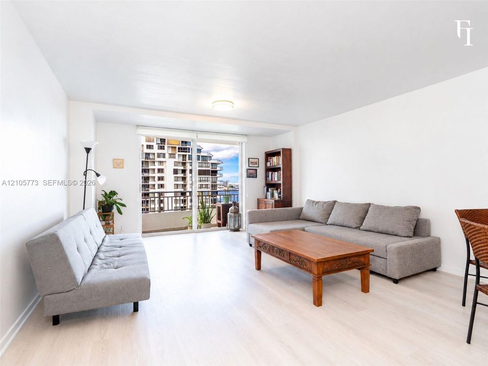 Open-concept living space featuring wood-finish flooring and floor-to-ceiling glass sliding doors providing access to a private balcony