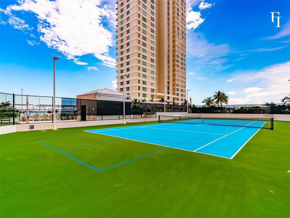 Multi-use sports court featuring a synthetic surface with integrated tennis net, perimeter fencing, and pole-mounted lighting