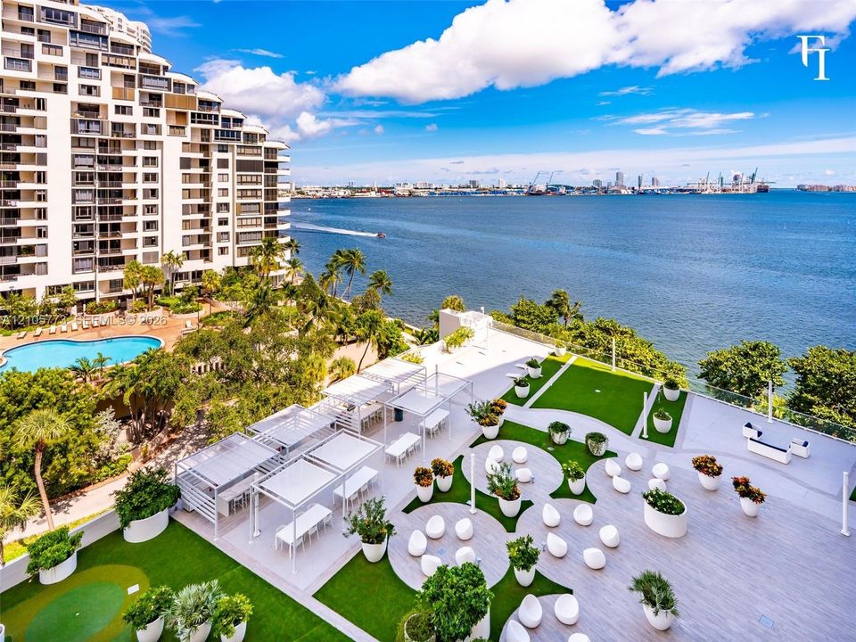 Expansive terrace featuring wood-finish decking, integrated artificial turf sections, overhead shade structures, glass railings, and a putting green