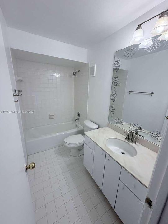 Bathroom featuring a vanity with an integrated countertop, oval sink, decorative mirror, three-light fixture, and a tiled shower-tub combination