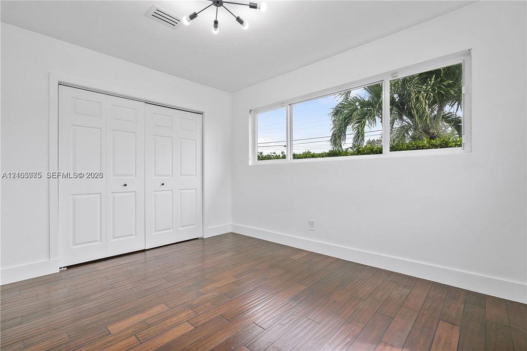 Room featuring dark-toned wood-finish flooring, a multi-arm modern light fixture, expansive horizontal window, and floor-to-ceiling built-in closet with dual paneled doors