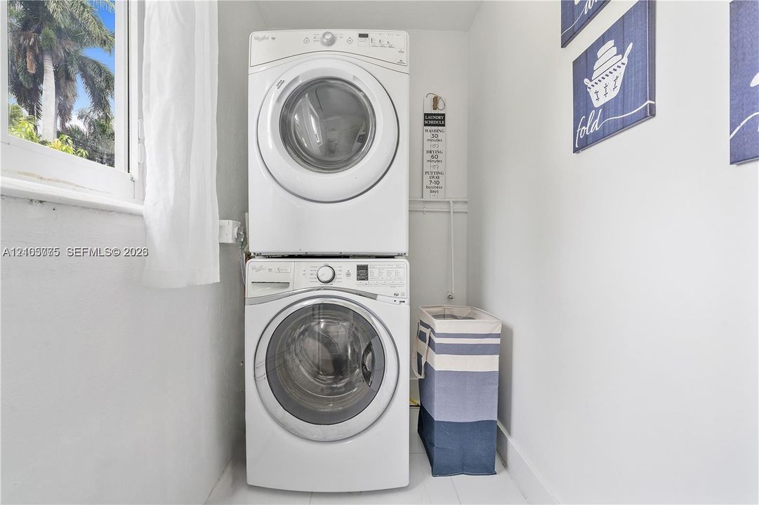 Dedicated laundry area featuring a white stackable front-load washer and dryer set and a window providing natural light