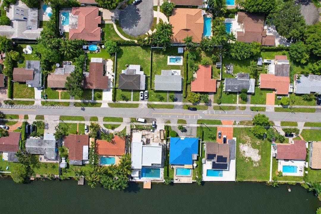 Aerial perspective of a waterfront residential neighborhood featuring multiple properties with private swimming pools and canal access