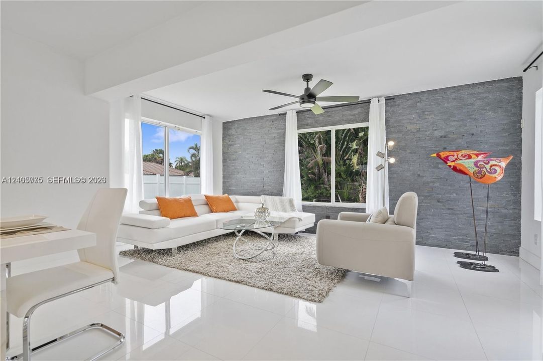 Living area featuring large-format tile flooring, a dark stone-finish accent wall, and a central ceiling fan