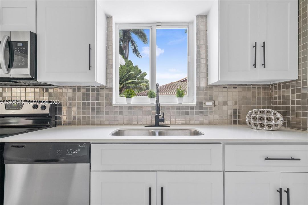 Kitchen featuring white shaker-style cabinetry, matte black hardware, stainless steel appliances, quartz countertops, and a metallic mosaic tile backsplash
