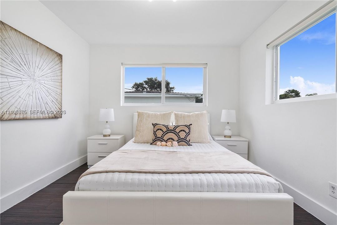 Room featuring dark wood-finish flooring, white walls, and two large windows