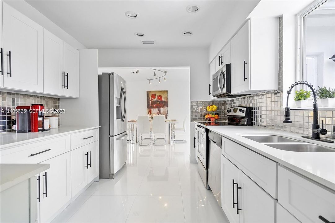 Kitchen featuring white shaker-style cabinetry, stainless steel appliances, tiled backsplash, dual-basin stainless steel sink with a matte black faucet, and polished tile flooring