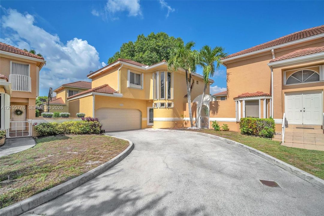 Stucco exterior featuring arched garage door, clay tile roofing, multi-pane bay windows, and private paved courtyard entrance