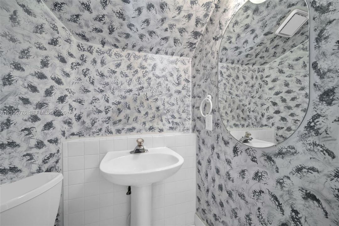 Pedestal sink with a single-handle faucet, white square-tiled wainscoting, and a frameless oval mirror