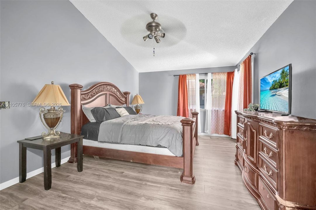 Vaulted ceilings featuring a centrally mounted ceiling fan and light fixture, complemented by neutral wall paint and wood-finish flooring