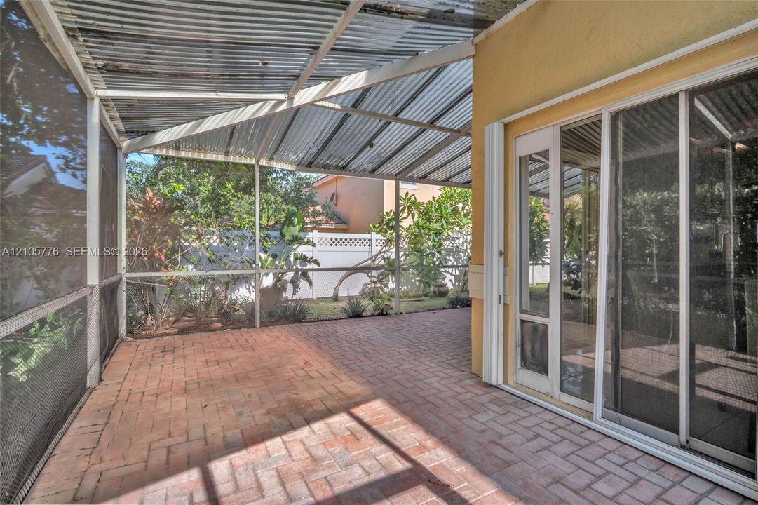 Screened-in patio featuring a corrugated metal roof, brick paver flooring, and sliding glass door access