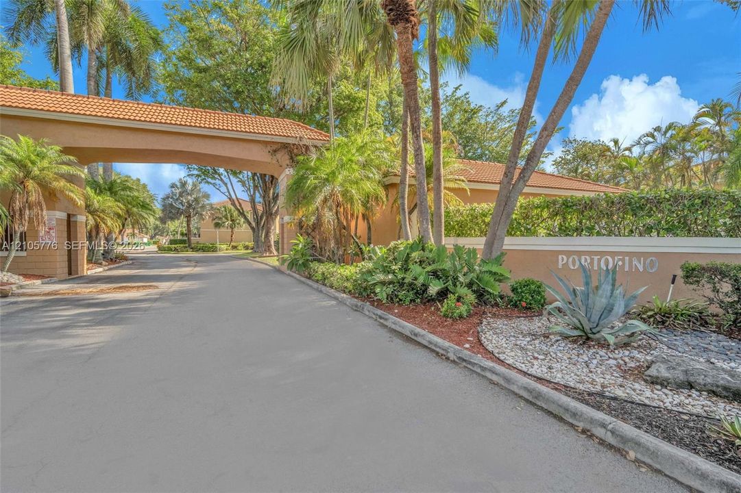 Gated entry featuring a stucco portico with terracotta tile roofing, mature palm trees, and professional xeriscaping