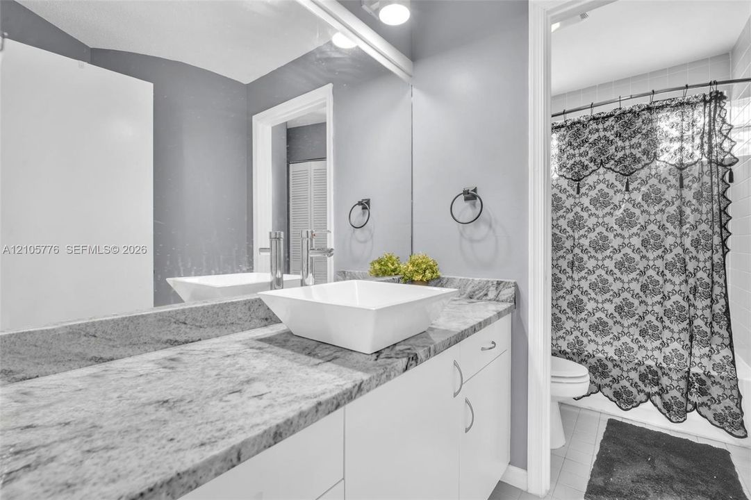 Stone-surface vanity featuring a white vessel sink, polished chrome faucet, full-width wall mirror, and white flat-panel cabinetry