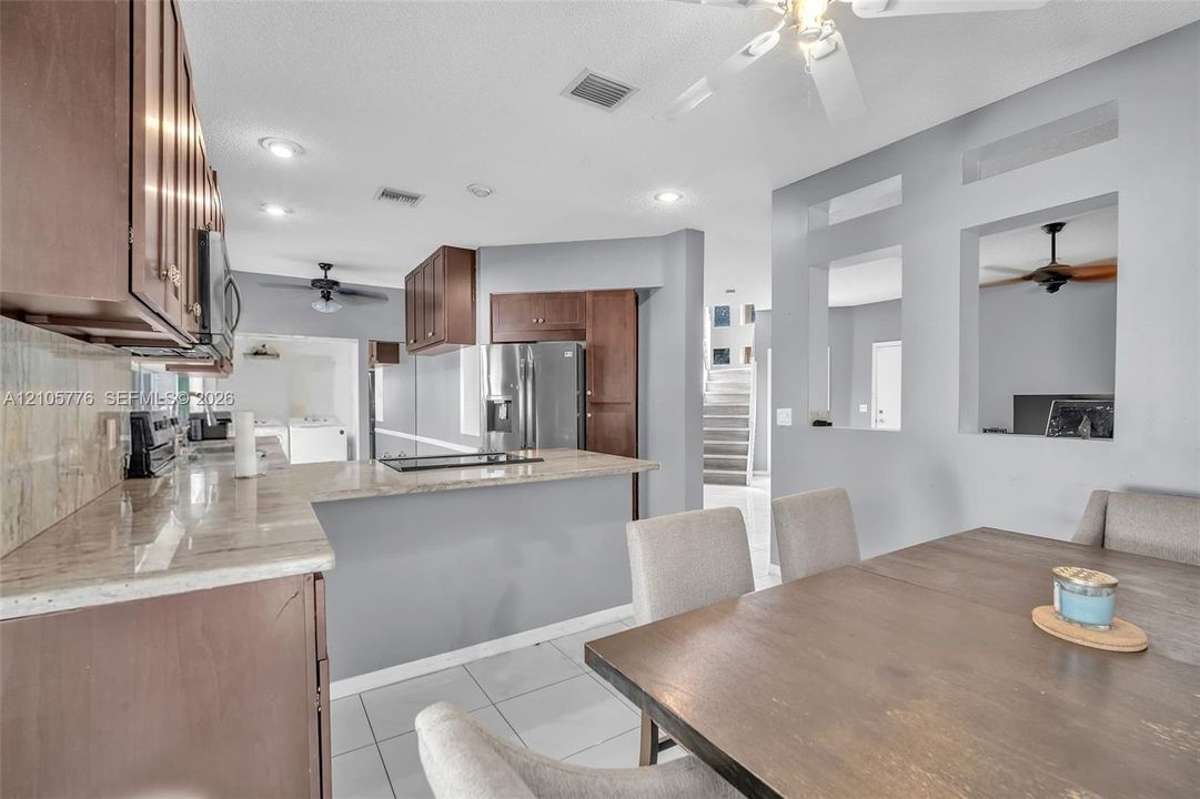 Kitchen featuring wood cabinetry, stone-surface countertops, integrated stainless steel appliances, recessed lighting, and tile flooring
