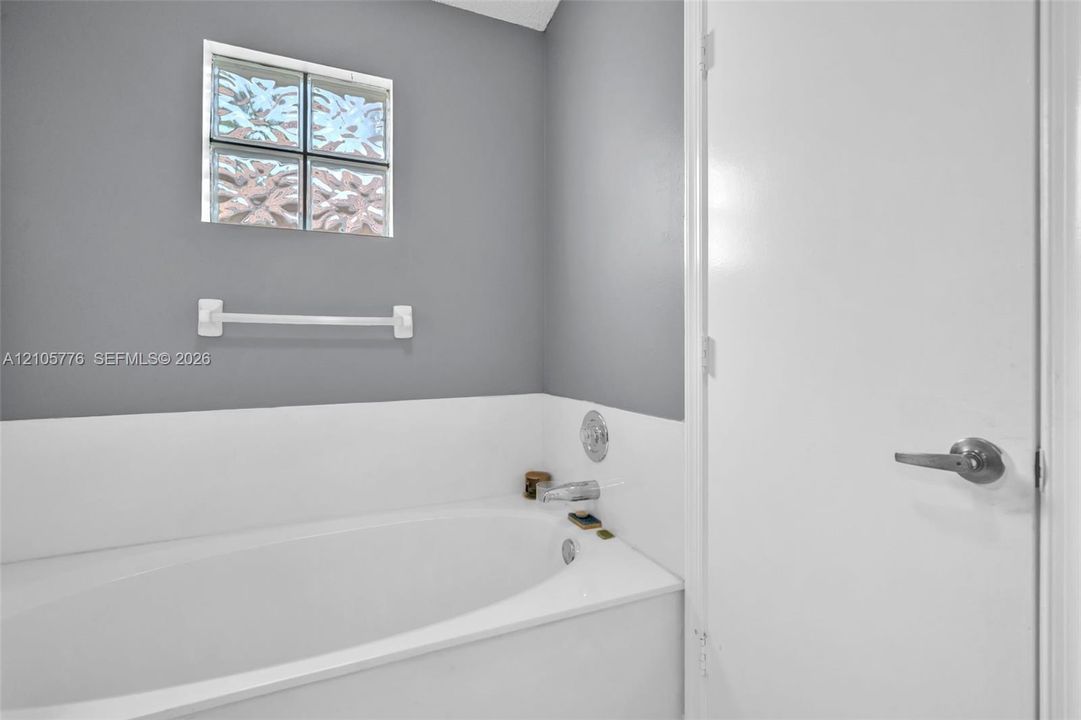 Built-in soaking tub with a white surround, glass block window, chrome faucet fixture, and mounted towel bar