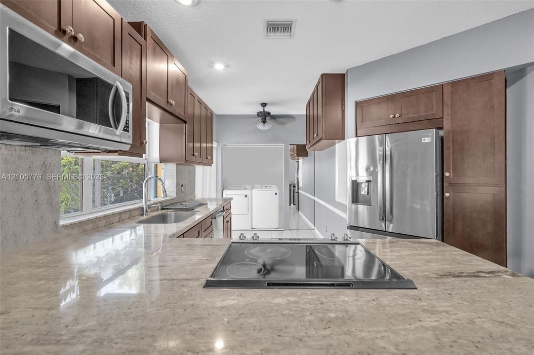 Kitchen featuring stained-wood cabinetry, stone countertops, integrated stainless steel appliances, and a cooktop set within the island