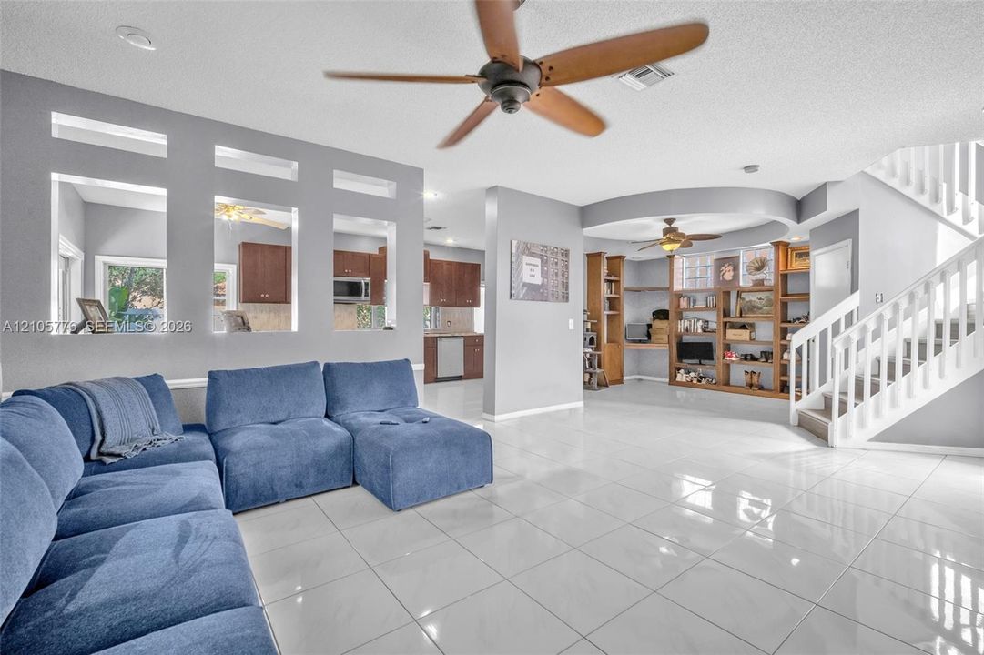 Living space featuring high-gloss tile flooring, built-in wooden shelving, a decorative arched ceiling detail, recessed lighting, and a ceiling fan