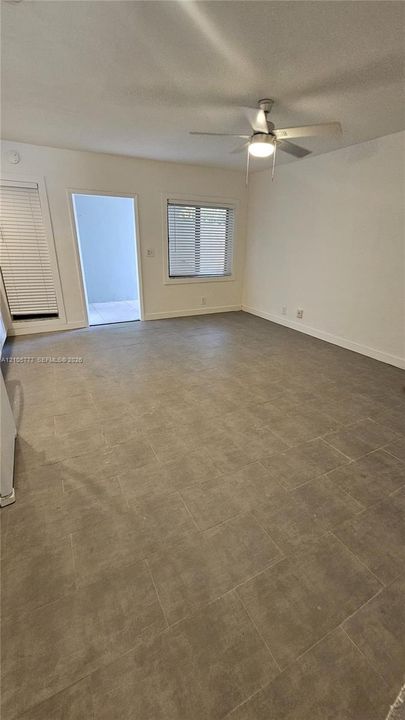 Large format tile flooring, ceiling fan with integrated light fixture, dual windows with horizontal blinds, and a private exterior doorway