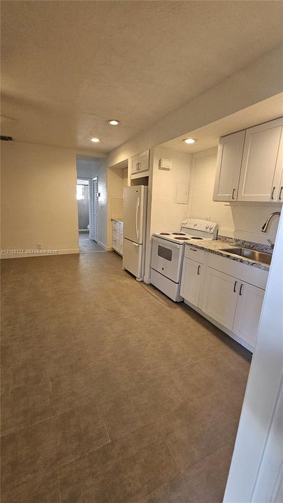 Kitchen featuring white shaker-style cabinetry, stone-finish countertops, stainless steel sink with high-arch faucet, white freestanding range, and tile flooring