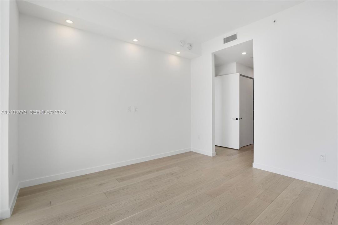 Neutral interior space featuring wood-finish flooring, recessed ceiling lighting, and a solid-core interior door with matte black hardware