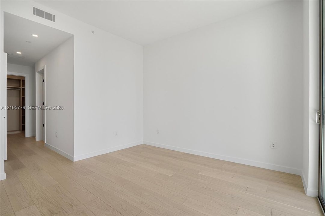 Neutral interior featuring light-tone wood-finish flooring, recessed lighting, and a walk-in closet with built-in shelving