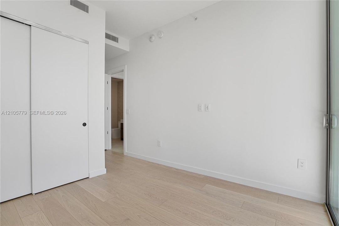 Interior space featuring light wood-finish flooring, sliding door closet, floor-to-ceiling glass paneling, and smooth-finish white walls