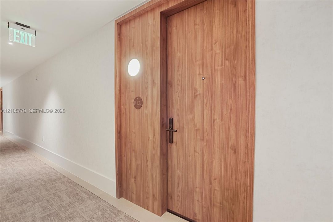 Wood-finish door with a matte black lever handle and integrated peephole, set within a wood-grain surround featuring a circular wall-mounted fixture