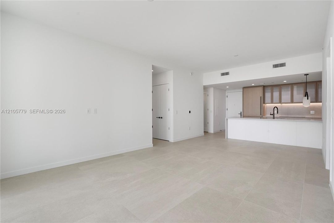 Open-concept interior featuring large-format tile flooring, kitchen with light wood cabinetry, integrated appliances, stone-surface counters, and matte black plumbing fixtures