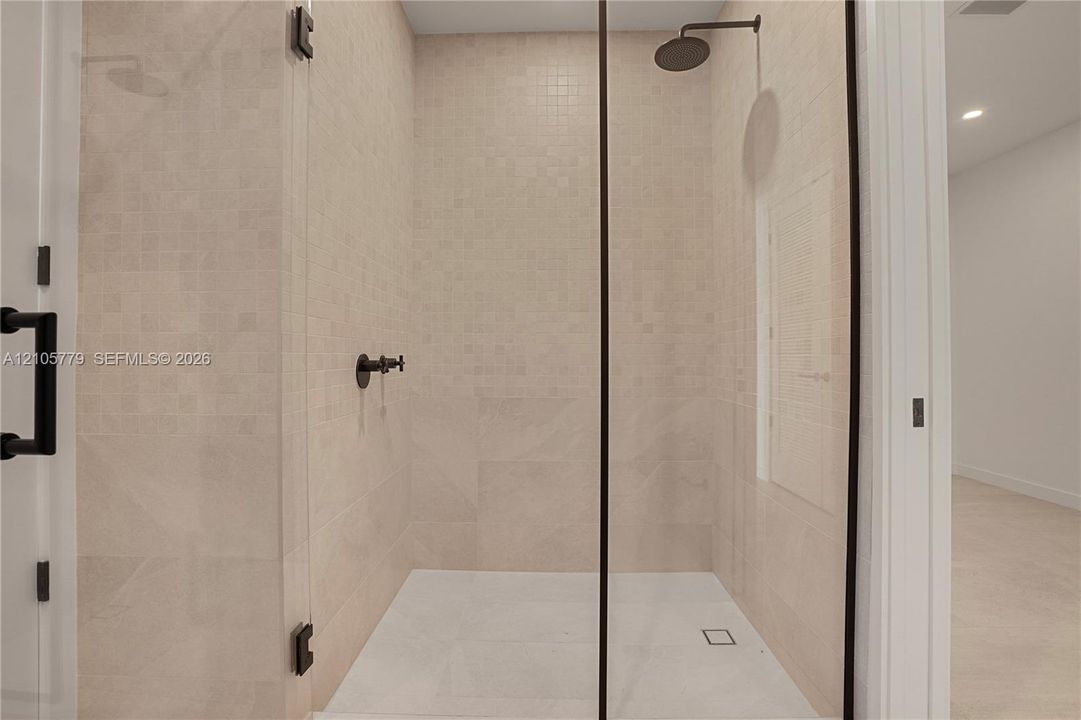 Walk-in shower featuring floor-to-ceiling neutral tile, glass enclosure with matte black hardware, rainfall showerhead, and wall-mounted matte black faucet