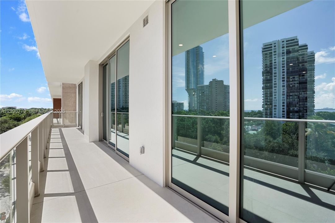 Expansive covered balcony featuring glass panel railings, floor-to-ceiling sliding glass doors, and neutral concrete-style flooring