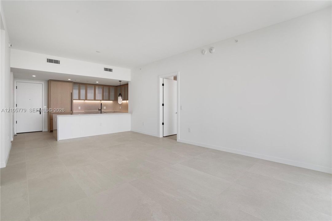 Open-concept interior with large-format neutral tile flooring, minimalist kitchen featuring light wood-tone cabinetry, stone-surface breakfast bar, and integrated cabinetry