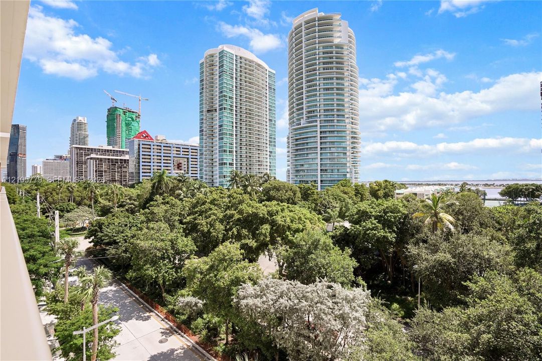 Exterior balcony featuring a concrete railing, mature tree canopy, and skyline backdrop