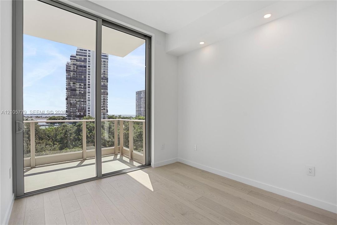 Floor-to-ceiling glass sliding door, balcony with railing, wood-finish flooring, and recessed ceiling lighting